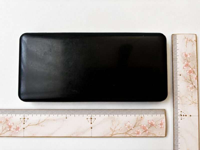 黒いモバイルバッテリーの縦横サイズを定規で測っている様子