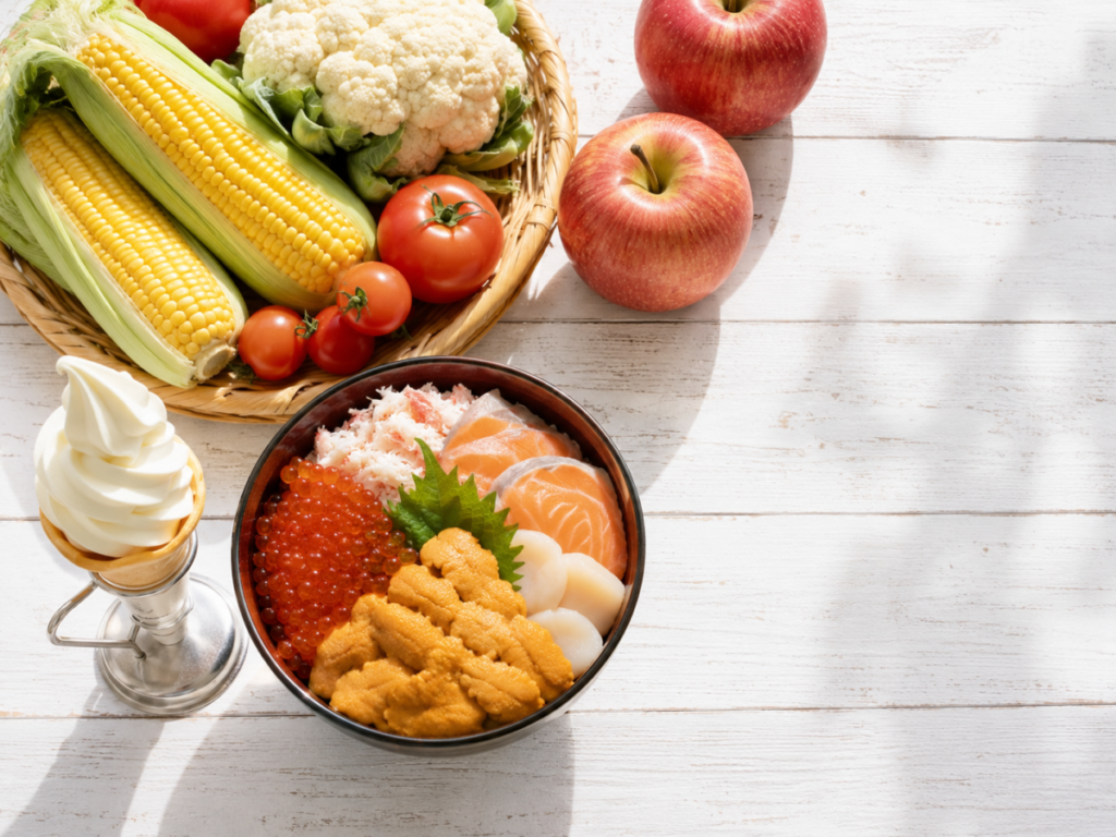 北海道の道の駅グルメをイメージした海鮮丼、夏野菜、ソフトクリーム、りんごが並ぶテーブル