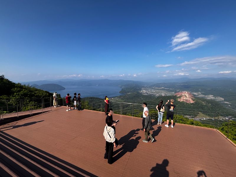 洞爺湖展望台Mt.USUテラスのウッドデッキから洞爺湖と昭和新山を眺める観光客