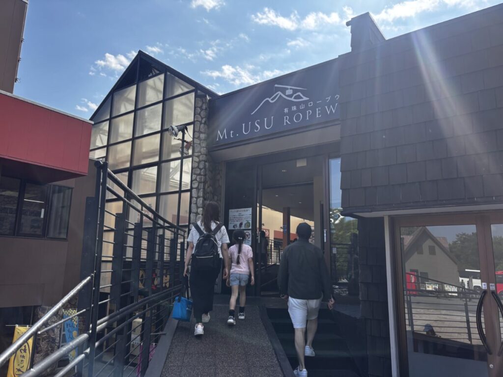 有珠山ロープウェイ山麓駅の入口へ向かう観光客とMt.USU ROPEWAYの看板