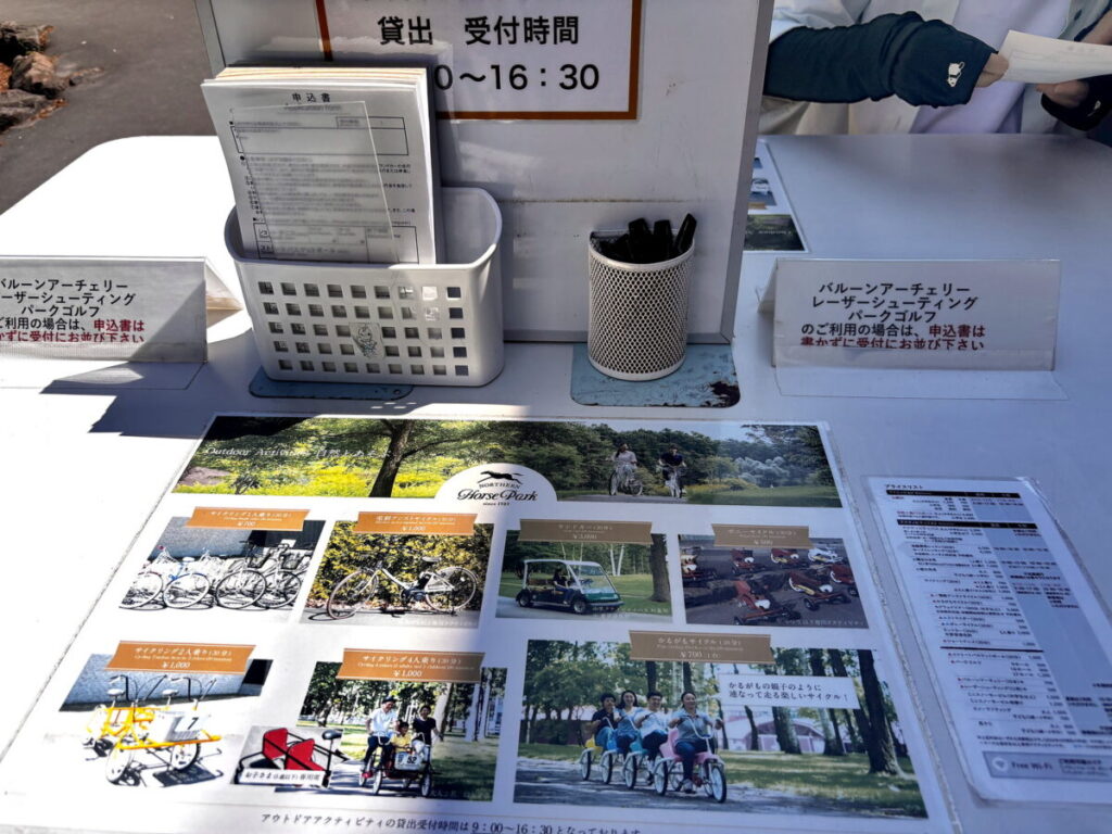 ノーザンホースパークのアウトドアアクティビティ貸出受付。サイクリングやランドカーの料金表と申込書が並ぶ