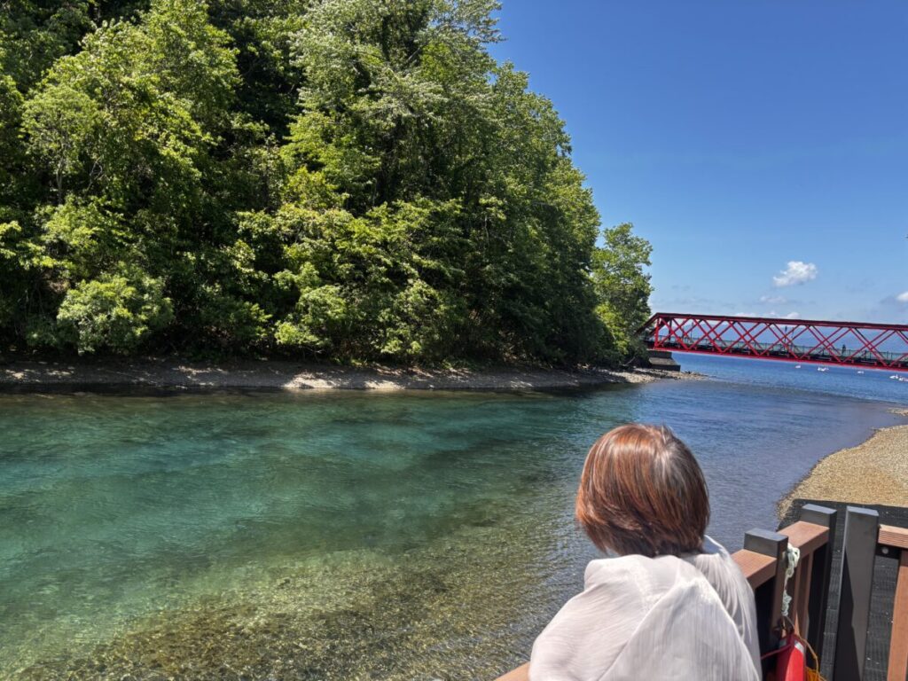 支笏湖から流れ出る千歳川の青い水面と山線鉄橋、青空を眺める女性の後ろ姿