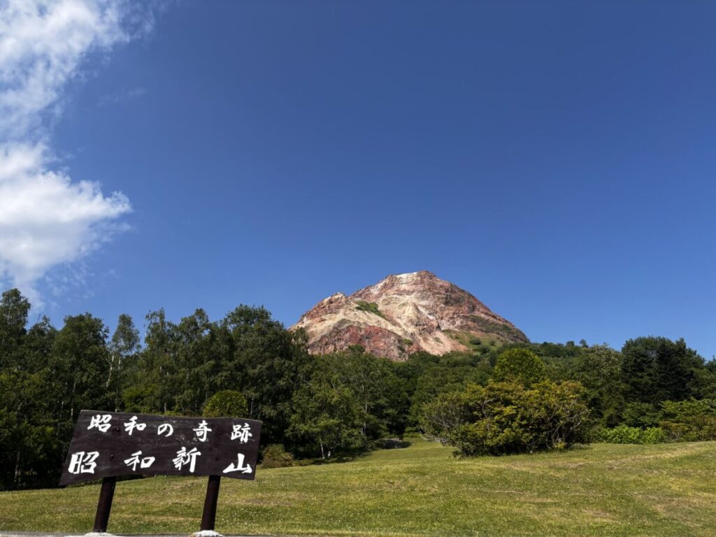 「昭和の奇跡 昭和新山」の看板越しに見る赤茶けた山肌の昭和新山と青空