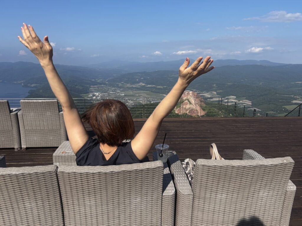有珠山Mt.USUテラスの椅子に座り絶景を眺めている女性が万歳している様子