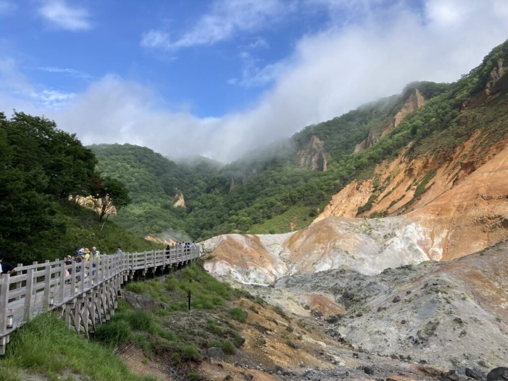 登別地獄谷の木道を歩く人たちと、湯けむりが上がる赤茶けた谷