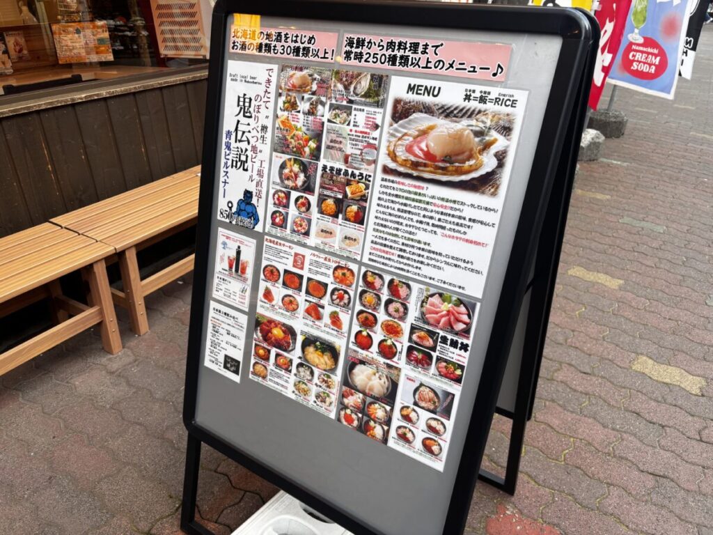 温泉市場の店頭メニュー看板、海鮮丼やホタテ料理の写真がずらりと並ぶ