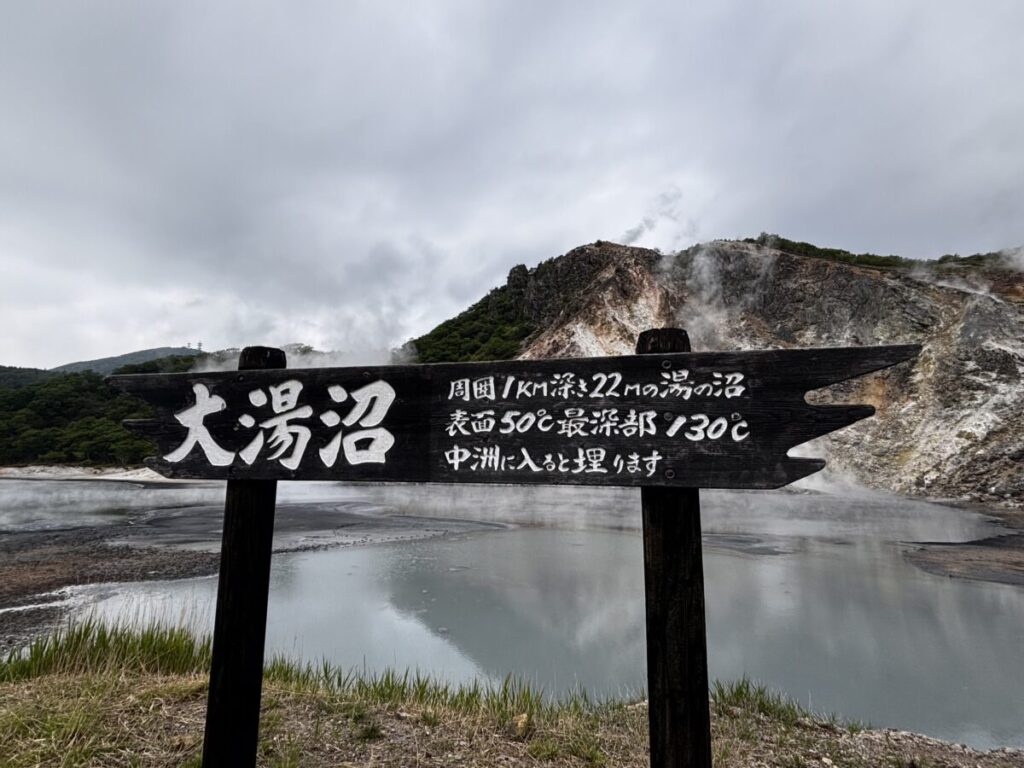 大湯沼の看板、周囲1キロ・最深部130度と記された案内と湯けむりの沼