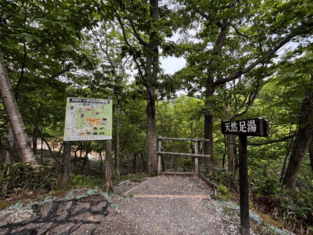 大湯沼川天然足湯の入口を示す木の看板と、地獄谷・大湯沼自然探勝路の案内図